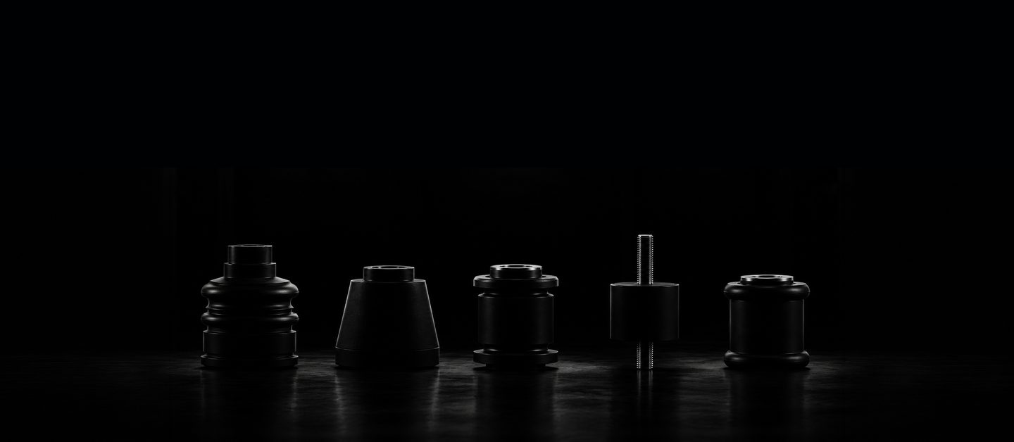 Five black rubber parts on a dark floor: a bellows boot, a cone mount, a flanged bushing, a stud mount and a bushing